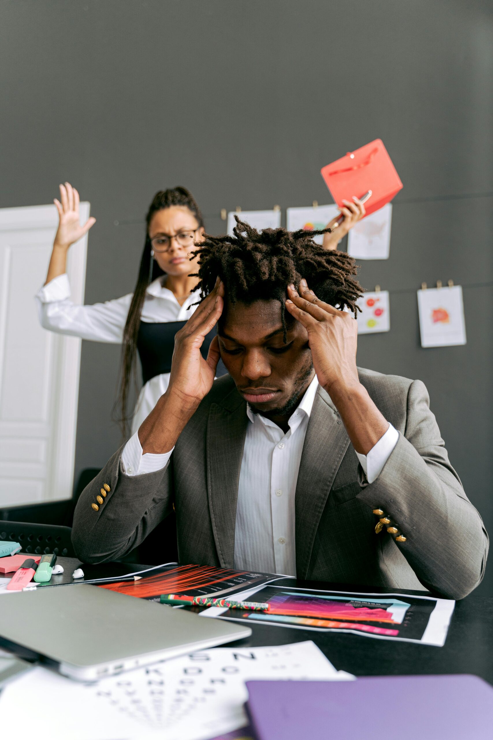 Frustrated businessman with dreadlocks dealing with stress at work while a colleague observes.
